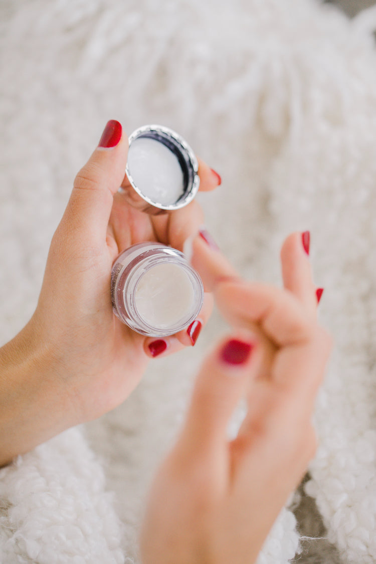 Mains au vernis a ongle rouge qui tient un pot de cosmétique